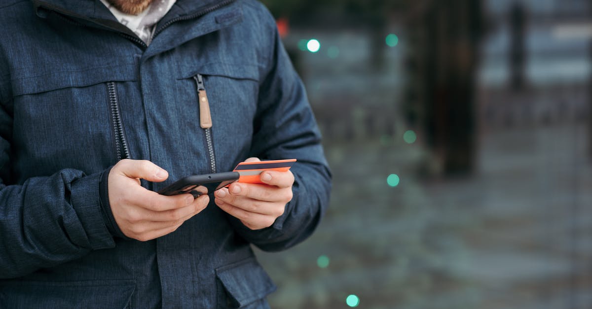 Can I travel using someone else's credit card? - Man browsing smartphone and holding credit card on street Can I travel using someone else's credit card? - Man browsing smartphone and holding credit card on street