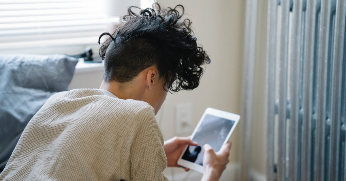 Can I watch YouTube on a domestic flight from London to Glasgow? - Unrecognizable young man with curly hair lying on bed and texting on tablet in weekend morning at home