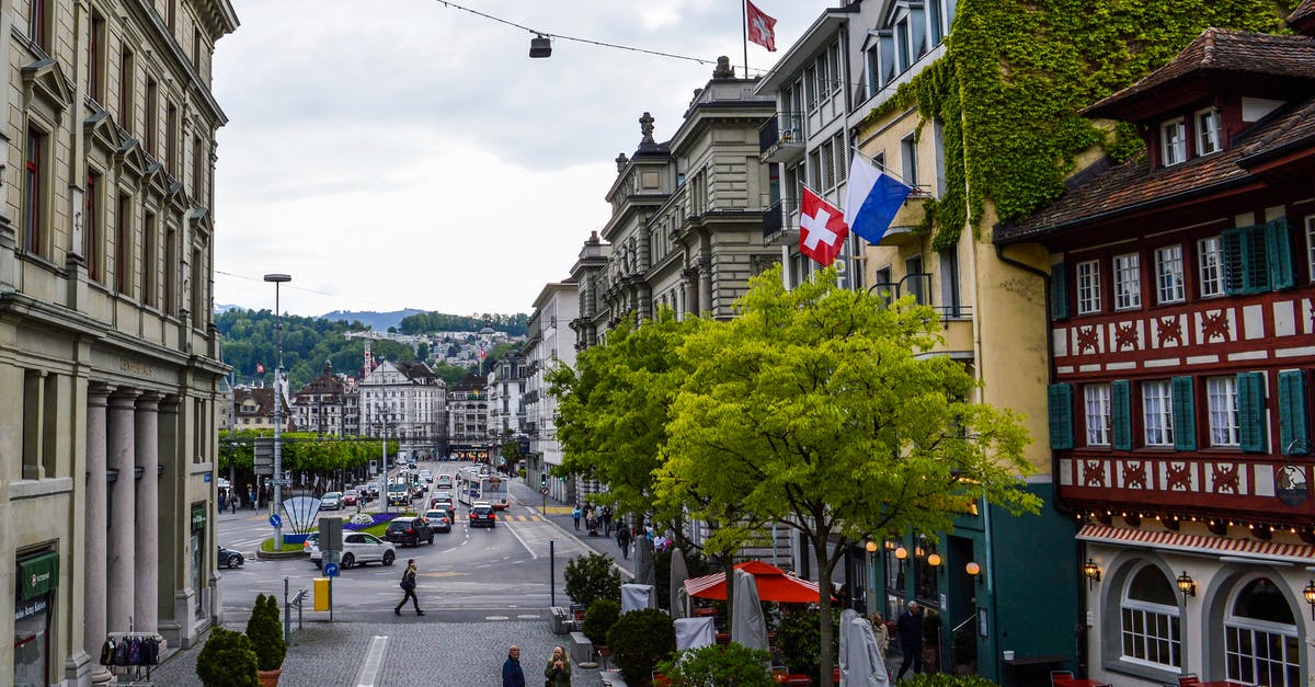 Can my family get a tourist visa for Switzerland from India - From above of old town with pedestrians walking among aged buildings with Switzerland flag Can my family get a tourist visa for Switzerland from India - From above of old town with pedestrians walking among aged buildings with Switzerland flag