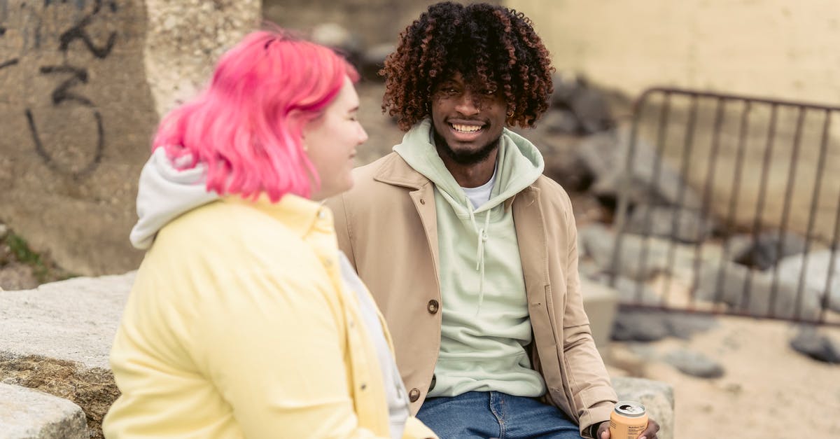 Can my Russian girlfriend leave the country if she owes the bank money? [duplicate] - Cheerful multiracial couple with cans of soda sitting on stones on embankment near river while spending time together during date