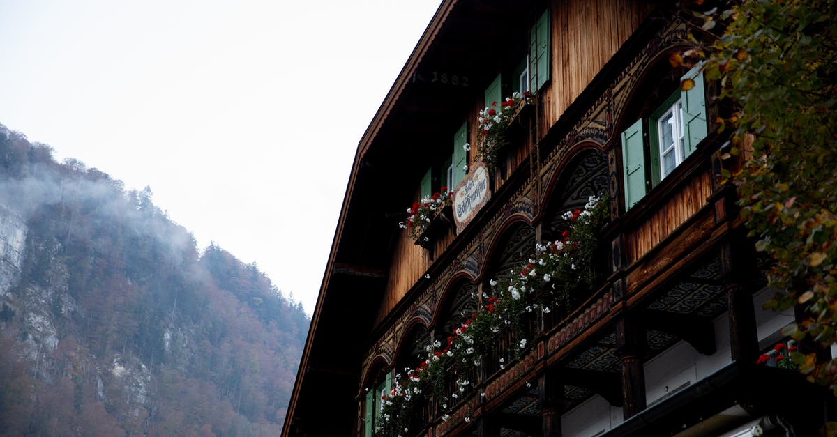 Can one apply for German visa from a country other than country of residence due to non availability of appointment - Facade of traditional wooden house decorated with colorful potted flowers located in quiet valley with forested mountains in cloudy weather