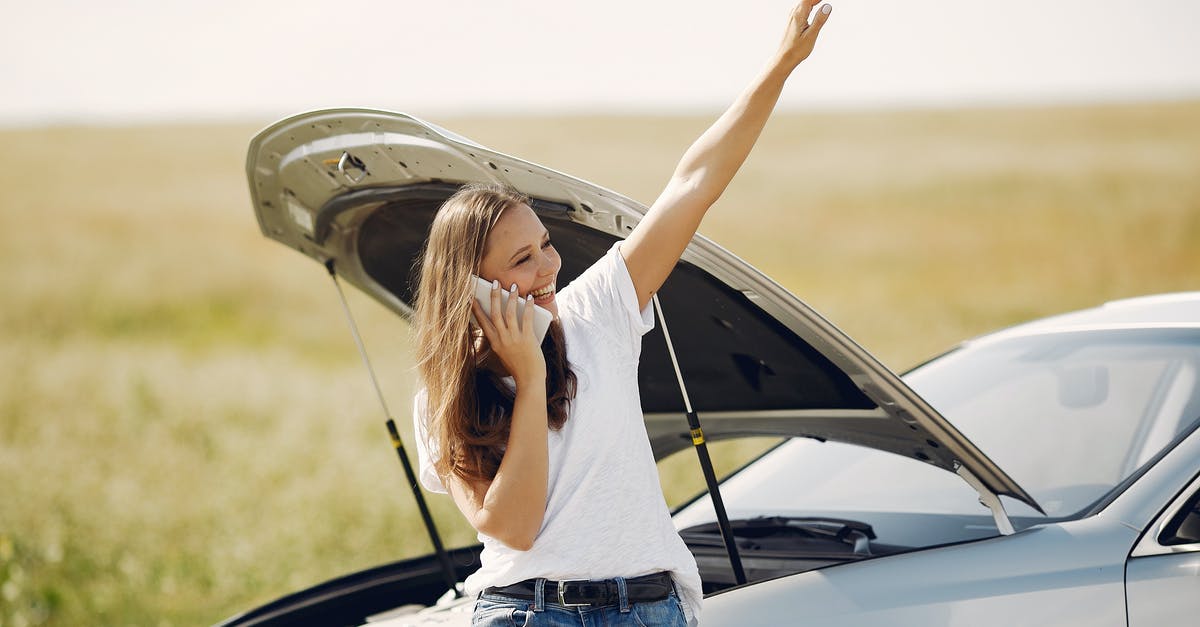 Can you get a gate pass at LAX to help someone who doesn't speak English? - Cheerful young female driver in white t shirt and jeans speaking on phone and looking away with smile while leaning on broken car with open hood and showing greeting gesture with raised hand