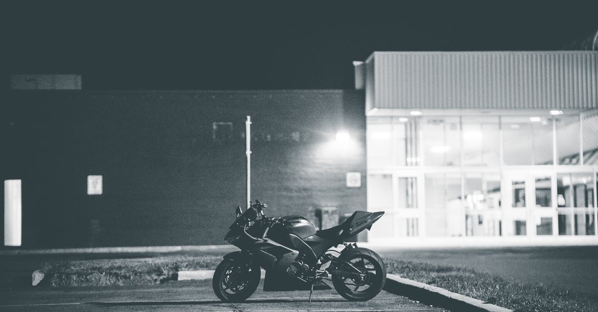 Canada: Entry by vehicle - Black and white of stylish motorcycle parked on asphalt surface on local street of city at night Canada: Entry by vehicle - Black and white of stylish motorcycle parked on asphalt surface on local street of city at night