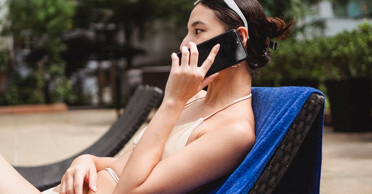 Cancellation fee for a hotel in Austria booked via phone call - Young slim ethnic lady talking on mobile phone while sitting on sunbed in hotel yard Cancellation fee for a hotel in Austria booked via phone call - Young slim ethnic lady talking on mobile phone while sitting on sunbed in hotel yard