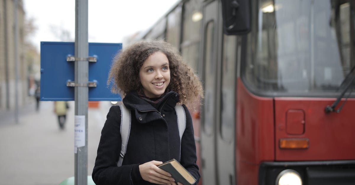 Cancelling only one passenger in a booking - Cheerful young lady with book waiting for bus on street Cancelling only one passenger in a booking - Cheerful young lady with book waiting for bus on street