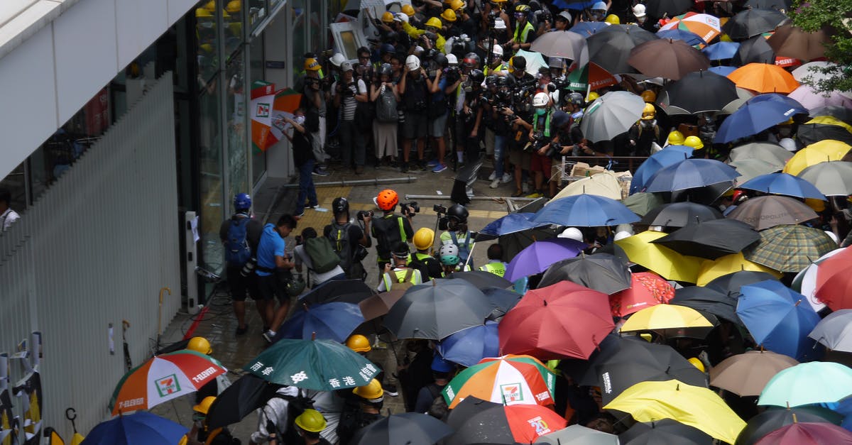 Central America, rain season and electronics - Crowded square with group of protestants near facade of building in rainy weather waiting in front of entrance Central America, rain season and electronics - Crowded square with group of protestants near facade of building in rainy weather waiting in front of entrance