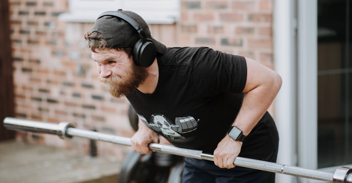 Change trains in Brest (Belarus) under 15 minutes? - Brutal male with headphones pulling massive metal barbell on blurred background of brick house Change trains in Brest (Belarus) under 15 minutes? - Brutal male with headphones pulling massive metal barbell on blurred background of brick house