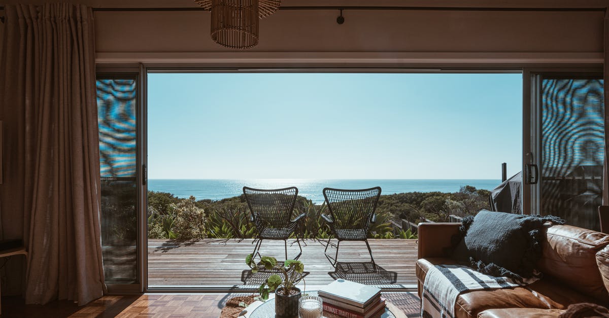 Cheap accommodation in Spain - Interior design of luxurious apartment with large balcony doors and wooden terrace having picturesque view on green forested seashore and calm blue sea Cheap accommodation in Spain - Interior design of luxurious apartment with large balcony doors and wooden terrace having picturesque view on green forested seashore and calm blue sea