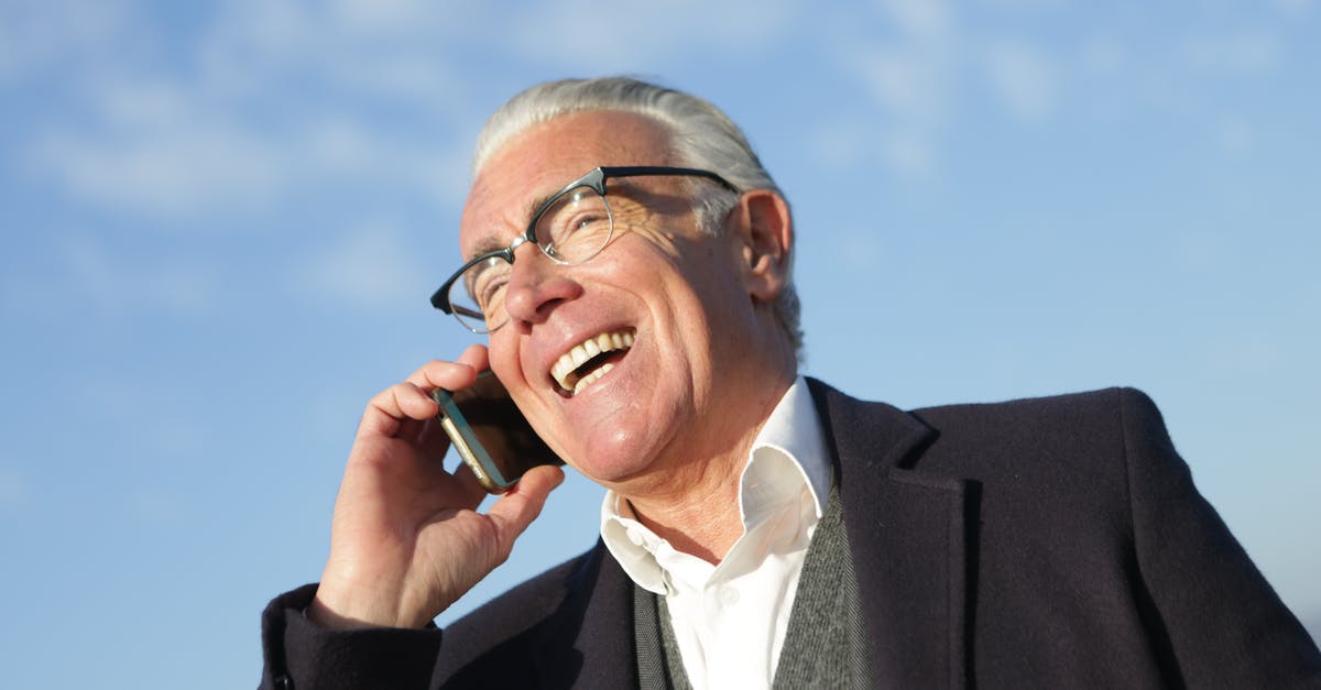 Cheap phone calls from Canada to Poland - From below of delighted aged male entrepreneur in classy outfit standing on street and speaking on cellphone while laughing and looking away Cheap phone calls from Canada to Poland - From below of delighted aged male entrepreneur in classy outfit standing on street and speaking on cellphone while laughing and looking away
