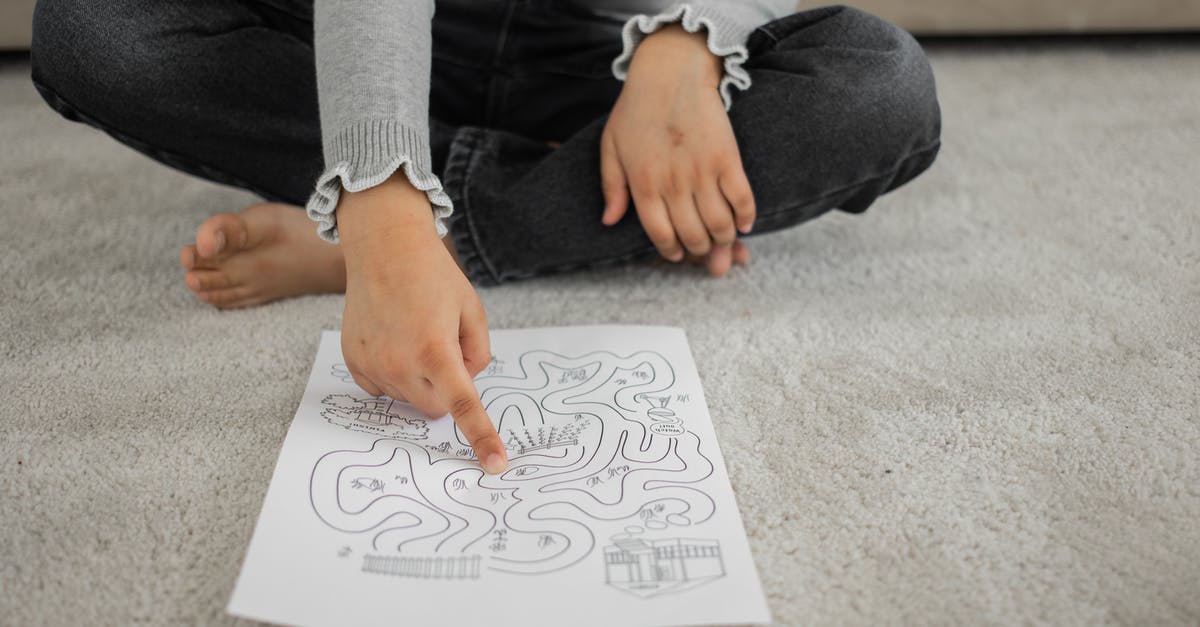 Cheap/free ski passes for children - Crop anonymous barefooted child sitting on floor with crossed legs and solving labyrinth puzzle at home
