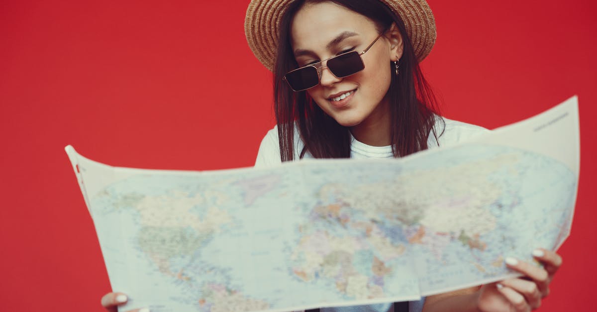 Checked baggage size limits - Smiling young woman in stylish hat and sunglasses choosing destination on paper map while standing with luggage on red background Checked baggage size limits - Smiling young woman in stylish hat and sunglasses choosing destination on paper map while standing with luggage on red background
