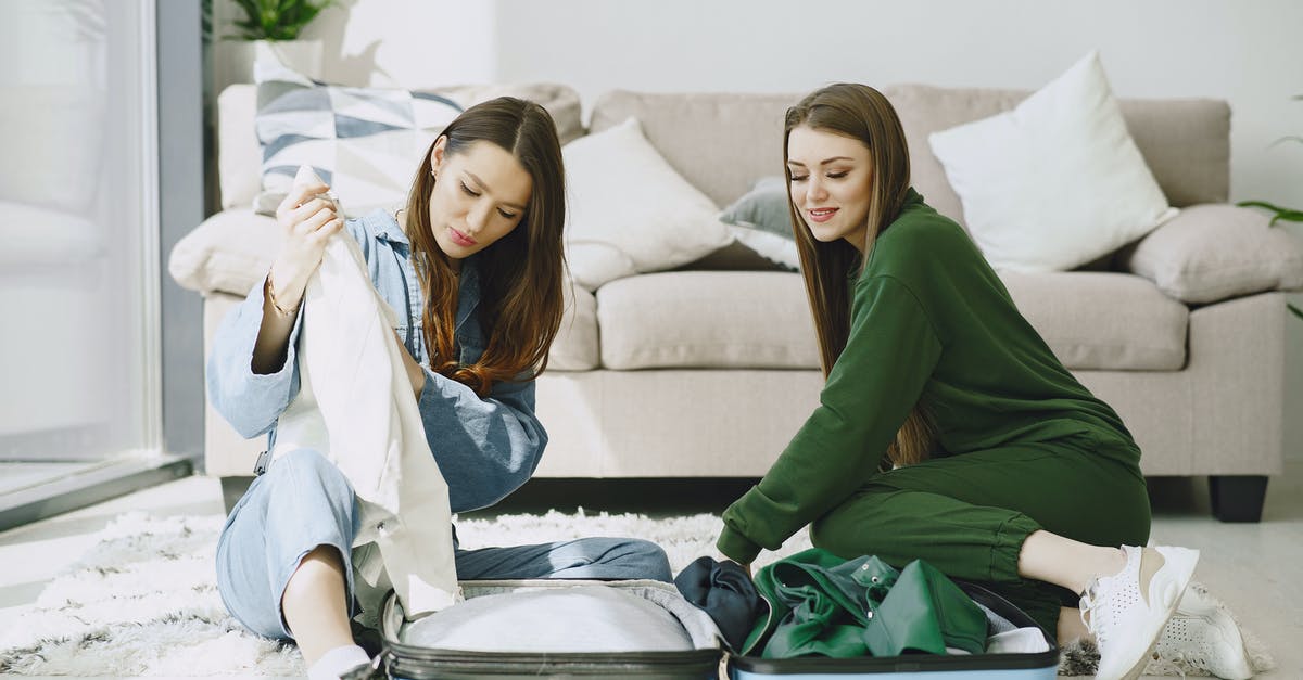Checked baggage tag-through service via several airlines (ORD, PVG, BKK) - Optimistic young female travelers in trendy outfits sitting on floor against comfortable sofa and unpacking suitcase in modern hotel room Checked baggage tag-through service via several airlines (ORD, PVG, BKK) - Optimistic young female travelers in trendy outfits sitting on floor against comfortable sofa and unpacking suitcase in modern hotel room