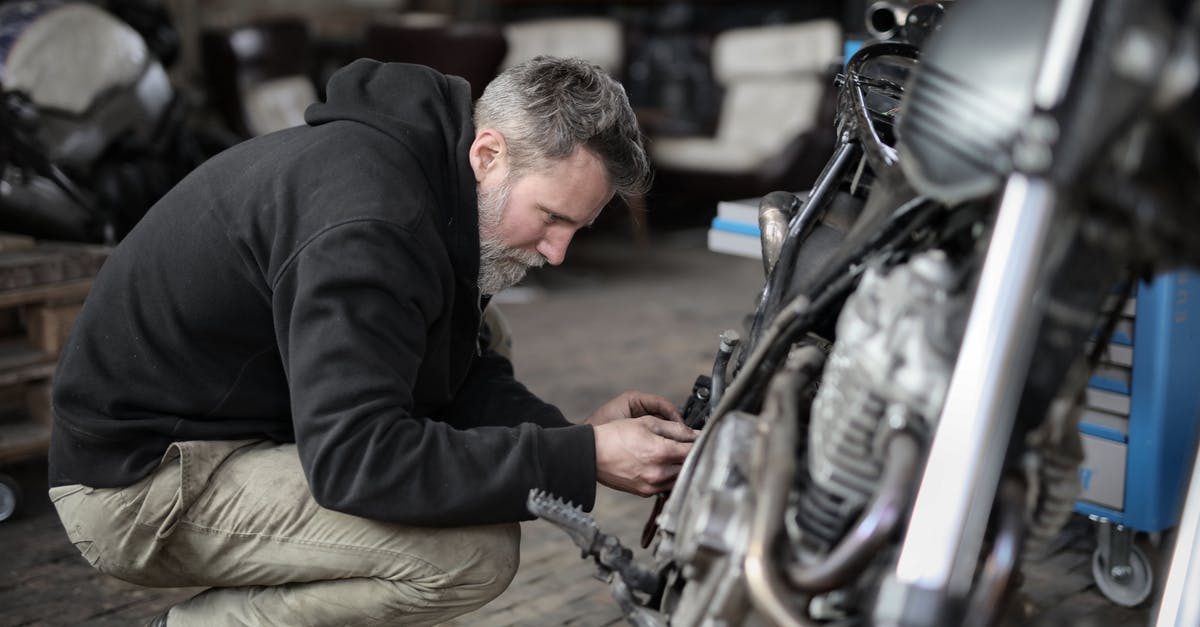 Checking a hire bike is properly docked - Side view of focused male mechanic in casual wear sitting near motorbike and examining details details in workshop Checking a hire bike is properly docked - Side view of focused male mechanic in casual wear sitting near motorbike and examining details details in workshop