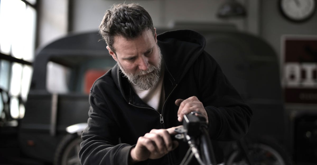 Checking a hire bike is properly docked - Concentrated male biker in casual wear fixing motorcycle part while working in garage Checking a hire bike is properly docked - Concentrated male biker in casual wear fixing motorcycle part while working in garage