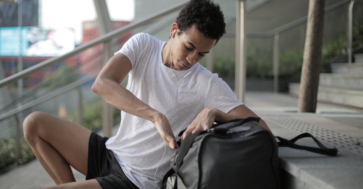Checking luggage for minor I'm not traveling with - Serious thoughtful African American man in earphones and sports clothes searching in bag pocket device while sitting on stairs and listening to music at entrance of contemporary building in downtown Checking luggage for minor I'm not traveling with - Serious thoughtful African American man in earphones and sports clothes searching in bag pocket device while sitting on stairs and listening to music at entrance of contemporary building in downtown