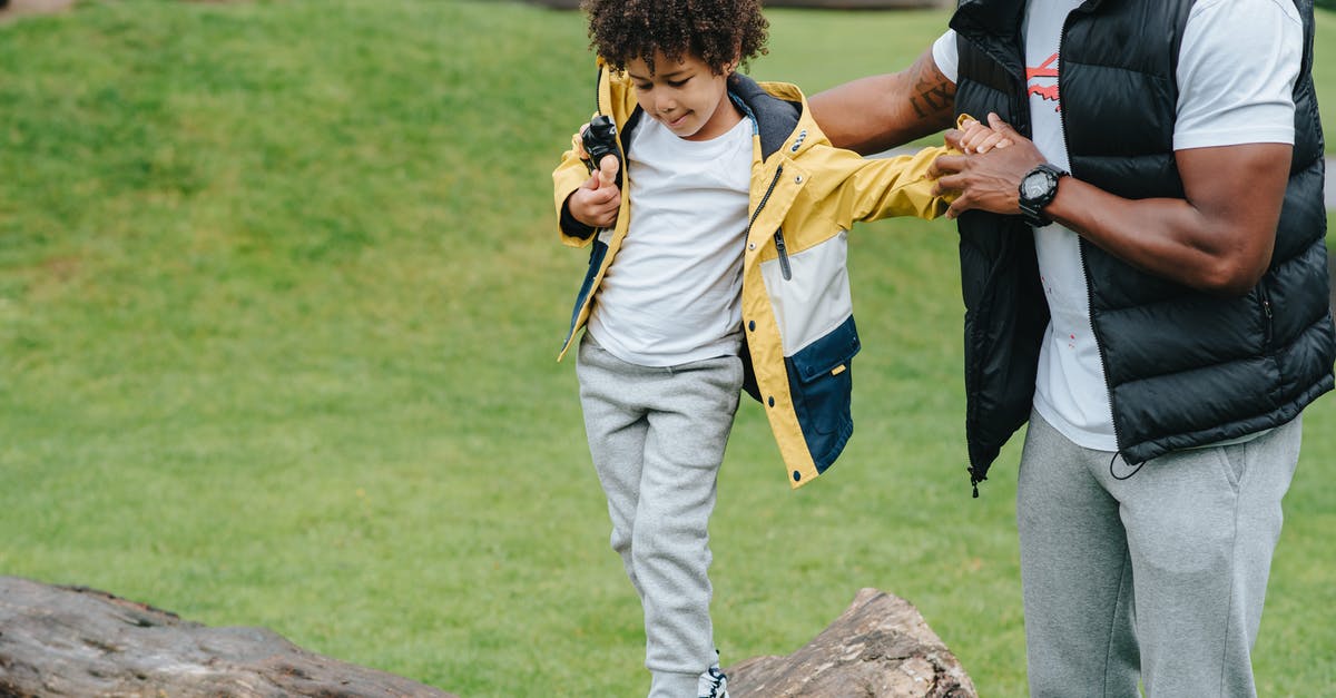 Checking MetroCard balance outside? - Caring African American man holding hands of careful kid while walking on wooden log in grassy park on blurred background Checking MetroCard balance outside? - Caring African American man holding hands of careful kid while walking on wooden log in grassy park on blurred background