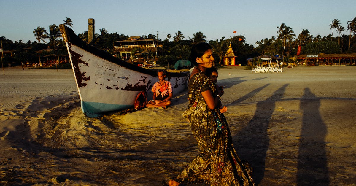 Child travel consent form for domestic travel within India - Indian woman carrying baby along sandy beach near shabby boat Child travel consent form for domestic travel within India - Indian woman carrying baby along sandy beach near shabby boat
