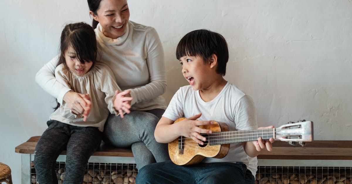 Children of U.K. Passport holder on accompaniment visas - Ethnic boy playing ukulele while sitting with mother and sister Children of U.K. Passport holder on accompaniment visas - Ethnic boy playing ukulele while sitting with mother and sister