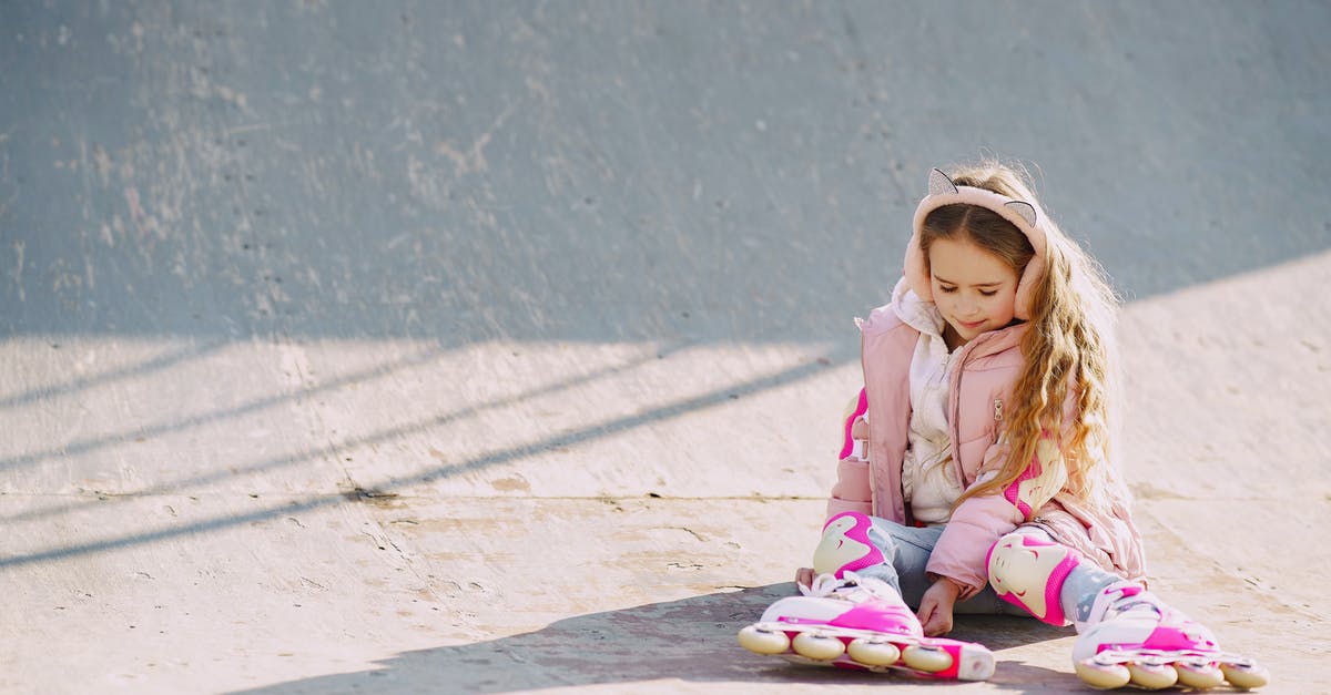 China visit visa for unaccompanied child [closed] - Glad little girl wearing warm pink jacket and protective pads looking down on rollers while sitting on concrete surface of ramp for skating during visiting skate park in sunny cold day