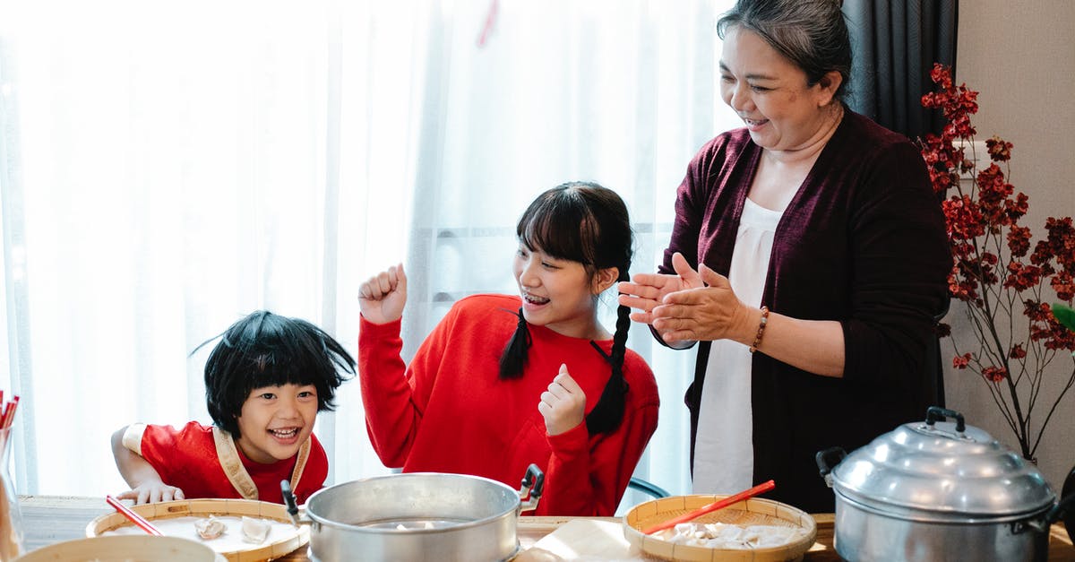 Chinese visiting England, have Schengen visa - Cheerful mature Asian woman with teenage granddaughter clapping hands while having fun with little boy helping with jiaozi preparation in kitchen Chinese visiting England, have Schengen visa - Cheerful mature Asian woman with teenage granddaughter clapping hands while having fun with little boy helping with jiaozi preparation in kitchen