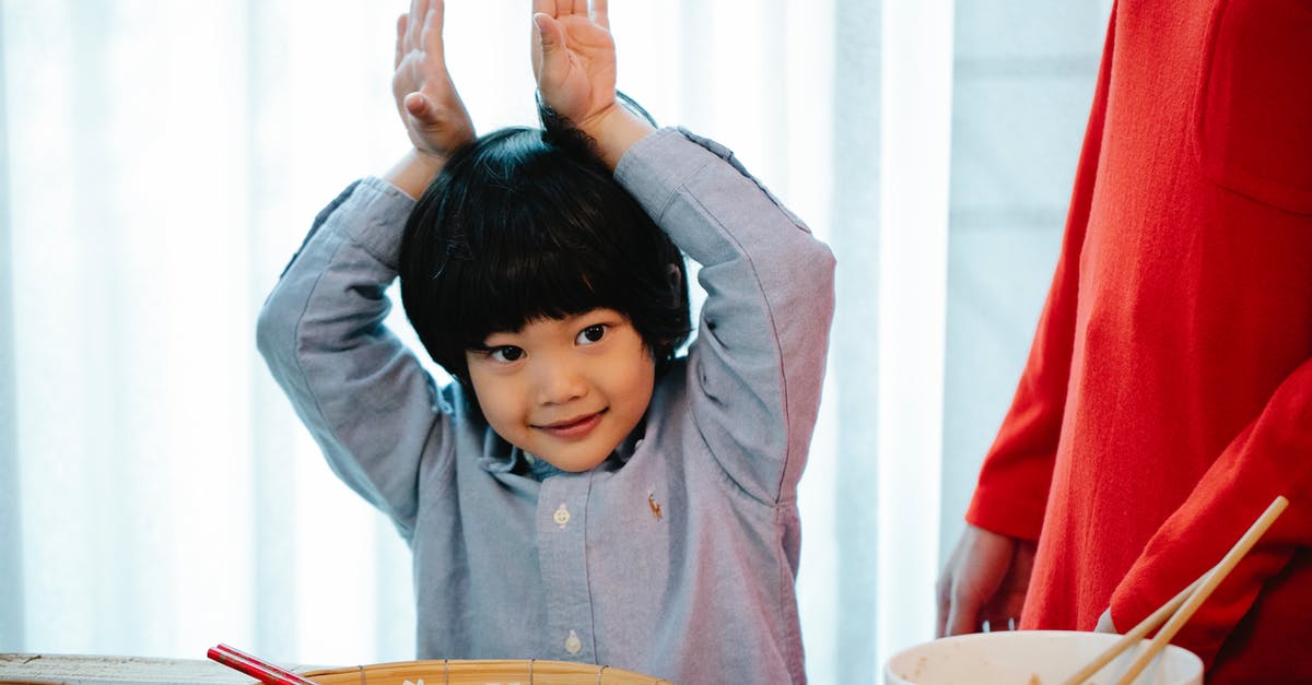 Chinese visiting England, have Schengen visa - Positive Asian kid making bunny ears with hands with hands in kitchen Chinese visiting England, have Schengen visa - Positive Asian kid making bunny ears with hands with hands in kitchen