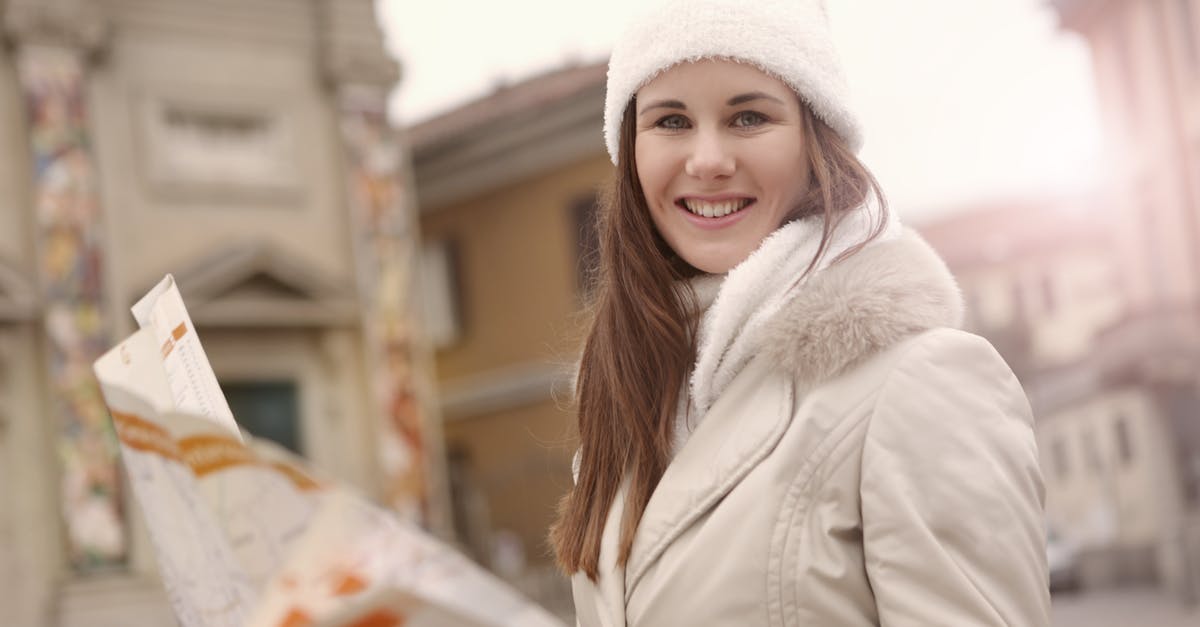 clothing required in Jungfrau tour in Oct 2016 [duplicate] - Young female tourist in warm jacket hat and scarf holding paper map and looking at camera while standing in historical center of city