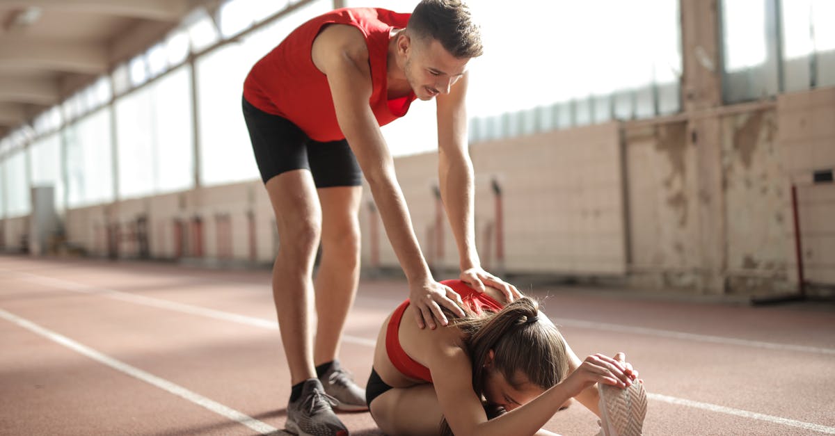 Coach platform positions for trains in Austria - Professional male sportsman helping woman touching knees with head while female sitting on running track and doing stretching exercise Coach platform positions for trains in Austria - Professional male sportsman helping woman touching knees with head while female sitting on running track and doing stretching exercise