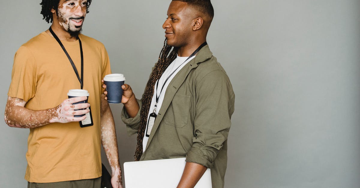 Company name spelled incorrectly - Black friends in casual clothes with name tags standing with cups of takeaway coffee on coffee break against gray wall