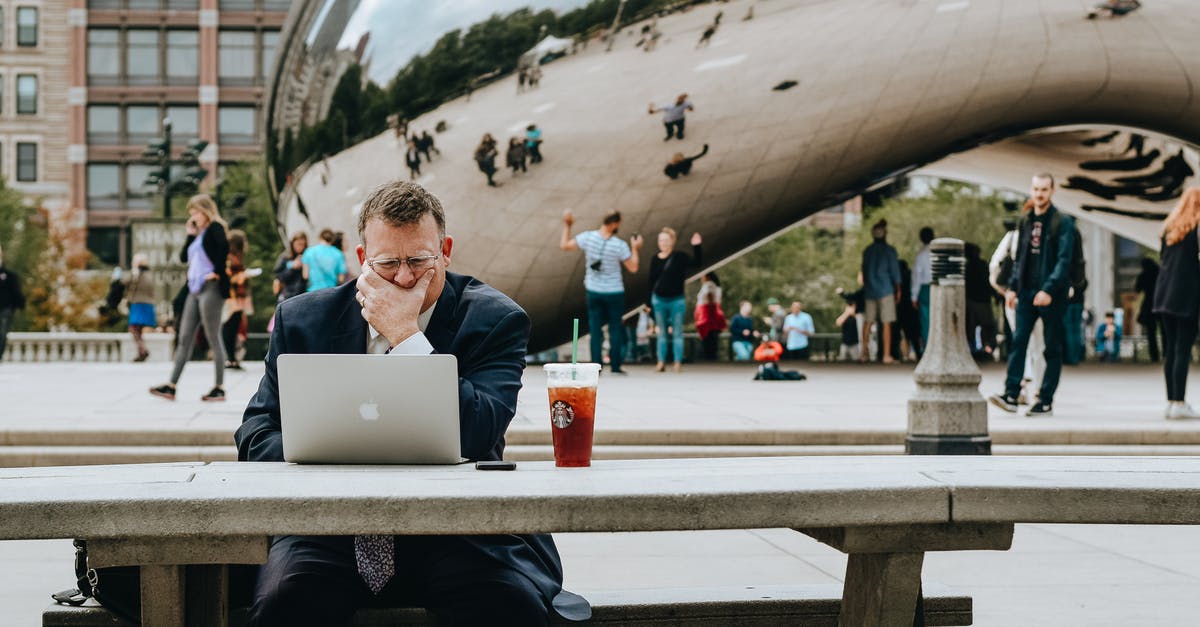 Connecting flight in Chicago - Concentrated businessman in suit touching face and sitting at table with laptop and takeaway drink against modern art sculpture Cloud Gate in Chicago in daytime Connecting flight in Chicago - Concentrated businessman in suit touching face and sitting at table with laptop and takeaway drink against modern art sculpture Cloud Gate in Chicago in daytime
