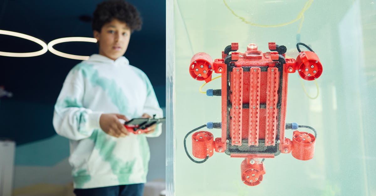 Connecting flight in Tel Aviv - From below of ethnic boy in hoodie controlling robot using panel while standing in light room Connecting flight in Tel Aviv - From below of ethnic boy in hoodie controlling robot using panel while standing in light room