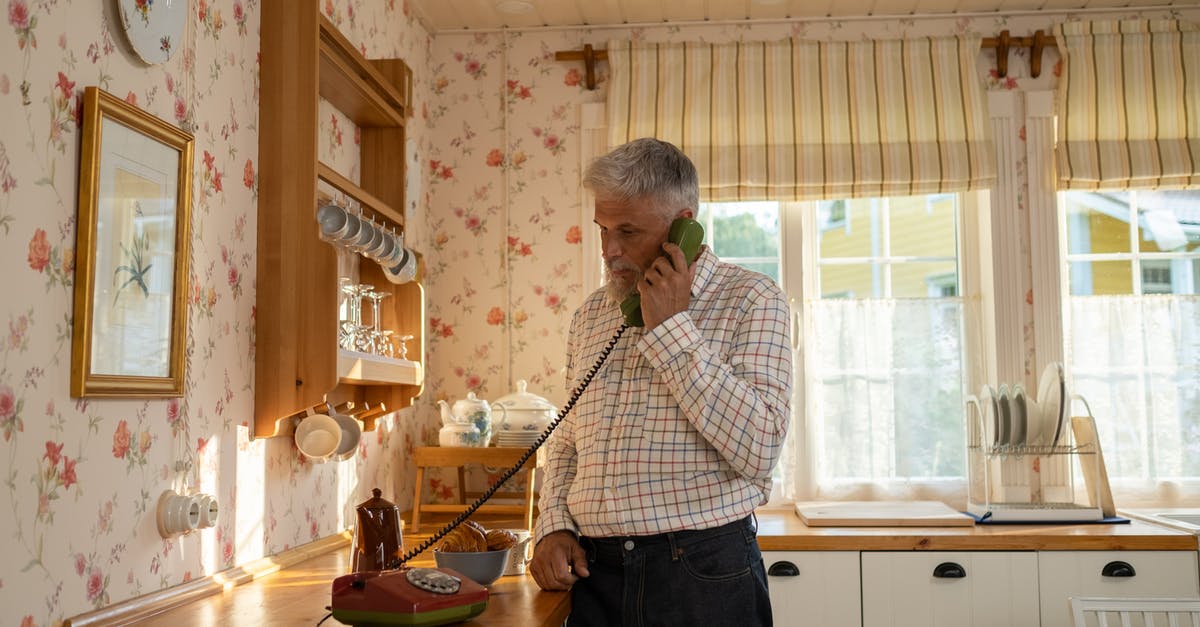 Connecting flights (domestic) on separate tickets with no checked baggage - Senior Man Talking on Landline Phone in Old-Fashioned Kitchen Connecting flights (domestic) on separate tickets with no checked baggage - Senior Man Talking on Landline Phone in Old-Fashioned Kitchen