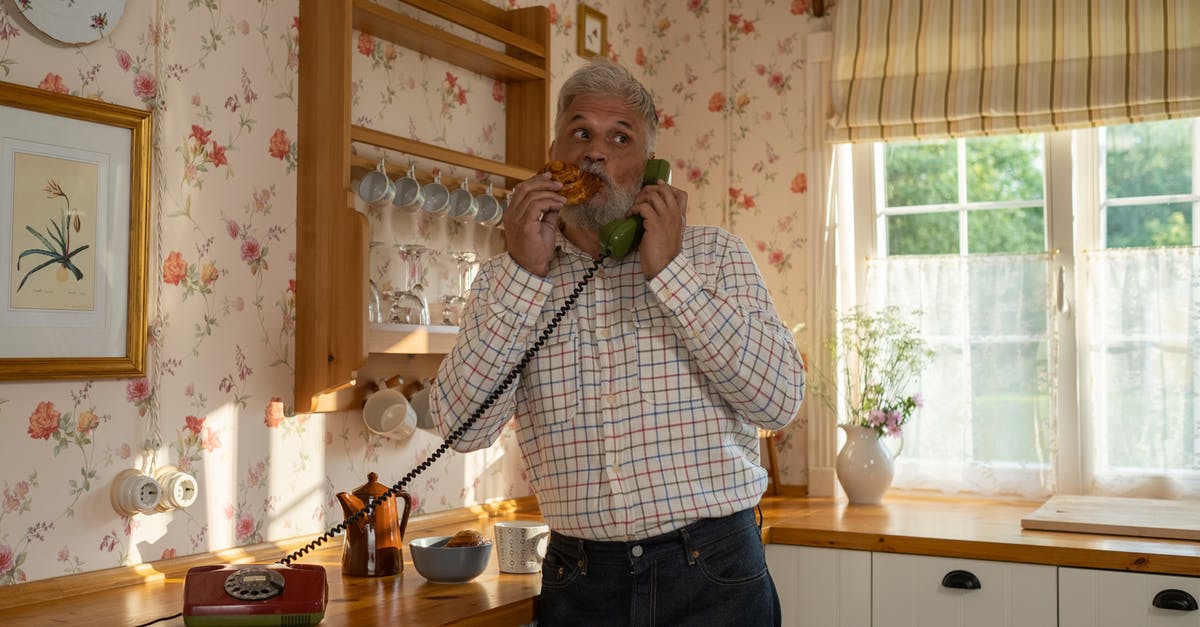 Connecting flights (domestic) on separate tickets with no checked baggage - Senior Man Talking on Landline Phone and Eating Cinnamon Bun in Old-Fashioned Kitchen Connecting flights (domestic) on separate tickets with no checked baggage - Senior Man Talking on Landline Phone and Eating Cinnamon Bun in Old-Fashioned Kitchen