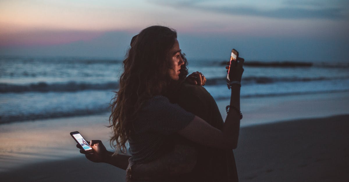 Connecting separate Airlines in Thailand - Couple hugging and using smartphone near sea on sunset Connecting separate Airlines in Thailand - Couple hugging and using smartphone near sea on sunset