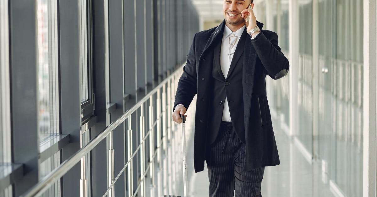 Connection in San Salvador, can I leave the airport and do some sightseeing? [closed] - Happy ethnic male in formal suit standing in modern hallway while holding suitcase in hand and talking on mobile phone