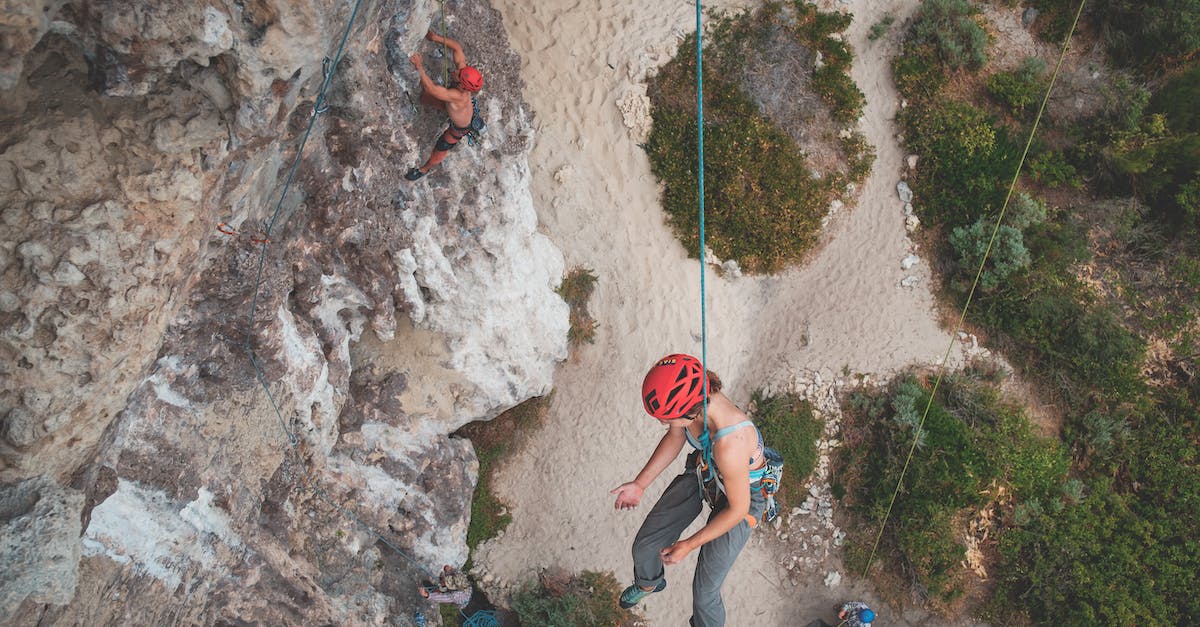 Coverage of unusual activities with travel insurance - From above of anonymous people hanging on ropes while climbing on stony cliffs with green bushes Coverage of unusual activities with travel insurance - From above of anonymous people hanging on ropes while climbing on stony cliffs with green bushes