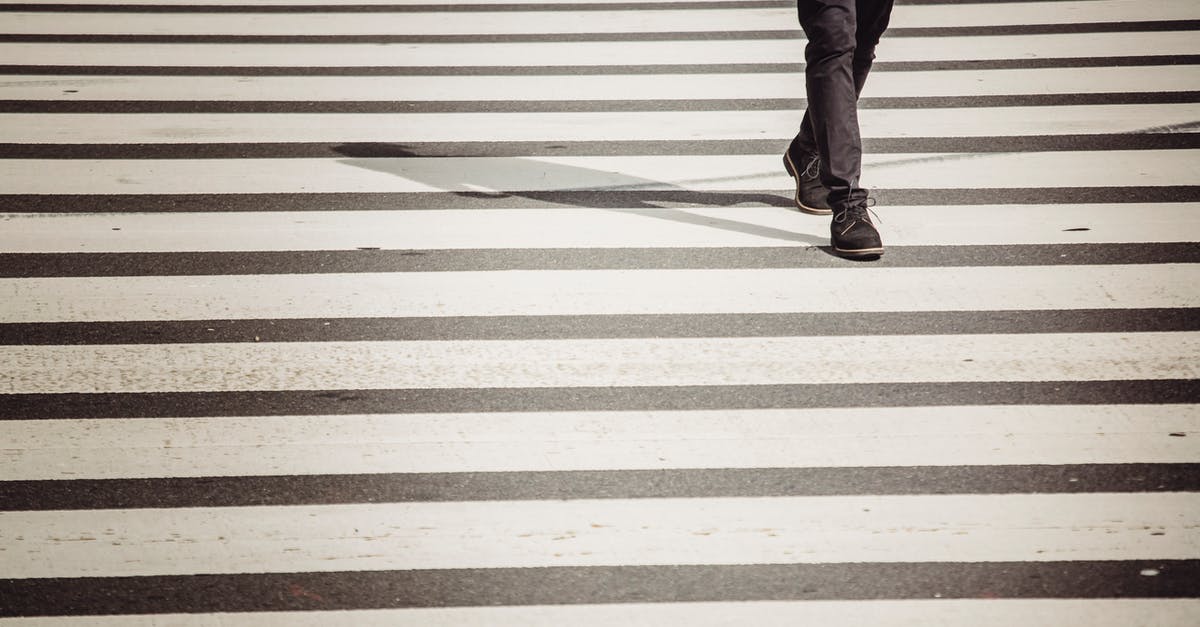 Crossing French-UK border under 18 alone - Crop anonymous black person in black trousers and shoes walking on zebra crossing in sunlight Crossing French-UK border under 18 alone - Crop anonymous black person in black trousers and shoes walking on zebra crossing in sunlight