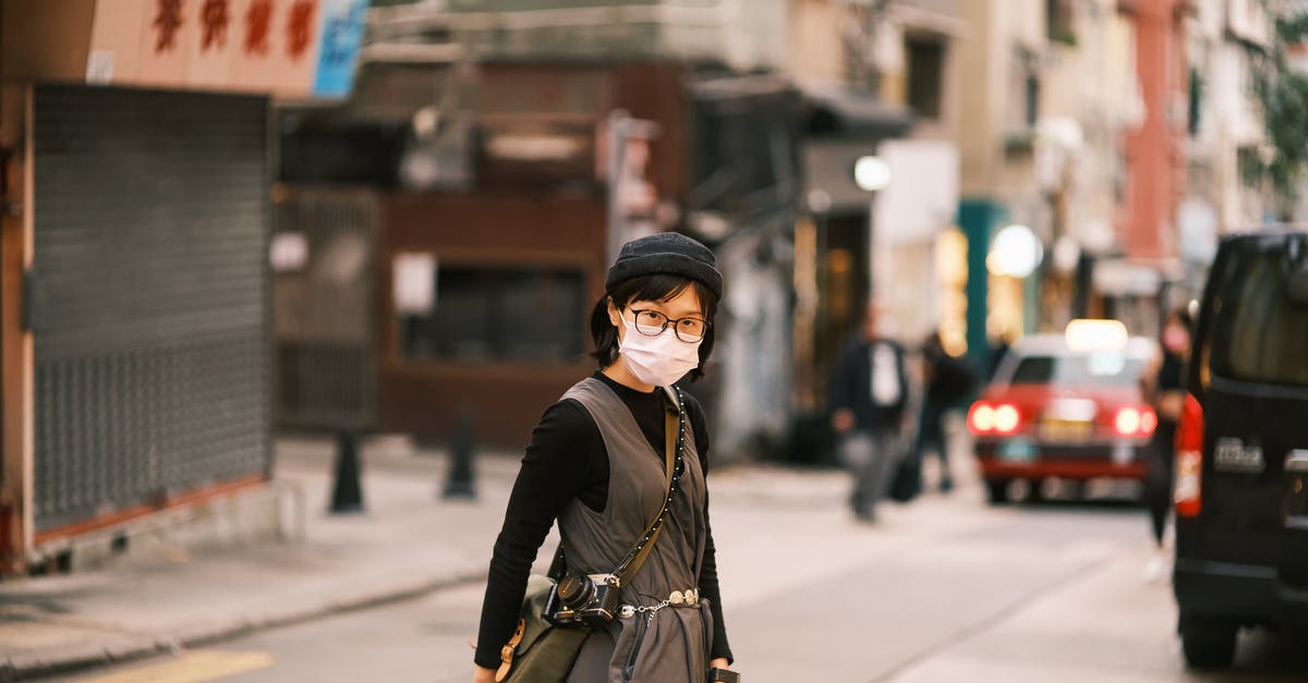 Crossing the Chinese border with a 50cc bike - Asian Woman in Specs and Face Mask Crossing Street in Chinese City Crossing the Chinese border with a 50cc bike - Asian Woman in Specs and Face Mask Crossing Street in Chinese City