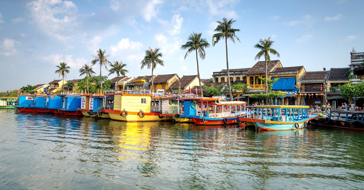 Cruising to Vietnam - Typical colorful boats moored on Thu Bon River near residential houses against blue sky in Hoi An Cruising to Vietnam - Typical colorful boats moored on Thu Bon River near residential houses against blue sky in Hoi An