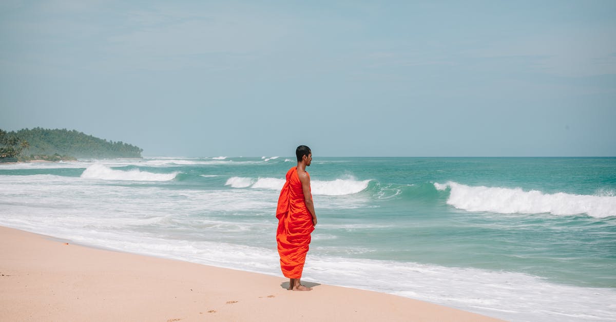 Culture Day in Osaka/Kyoto - Side view of full body young barefoot ethnic male Buddhist monk standing on wet sandy coast and admiring peaceful waving seascape during summer day Culture Day in Osaka/Kyoto - Side view of full body young barefoot ethnic male Buddhist monk standing on wet sandy coast and admiring peaceful waving seascape during summer day
