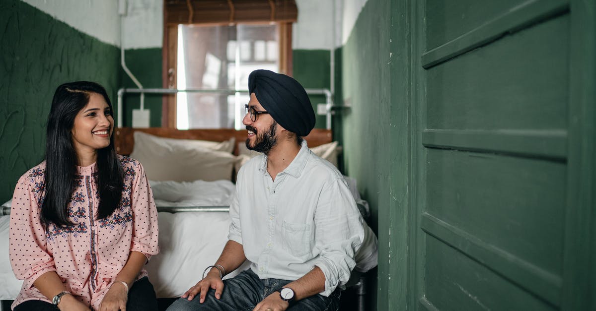 Date of arrival on an Indian e-visa - Smiling Indian couple in casual clothes and turban sitting on bench against bed in narrow green bedroom and chatting while looking at each other happily Date of arrival on an Indian e-visa - Smiling Indian couple in casual clothes and turban sitting on bench against bed in narrow green bedroom and chatting while looking at each other happily