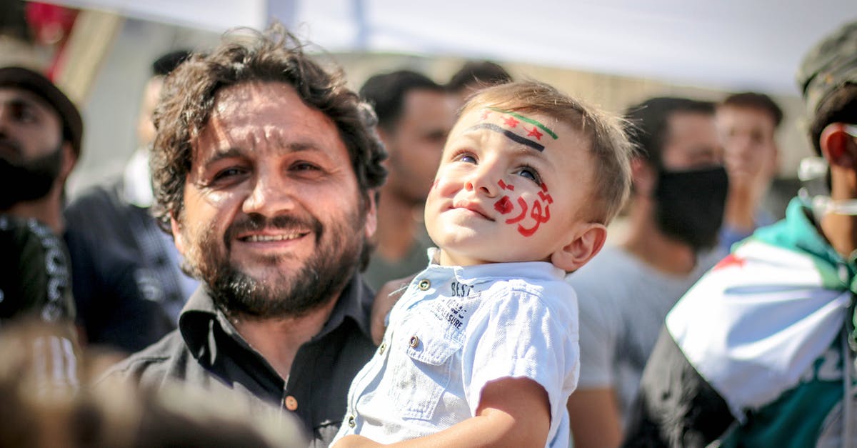 Delta carry-on policy - Ethnic bearded man carrying small kid with painted face in crowd of protesting against policy Delta carry-on policy - Ethnic bearded man carrying small kid with painted face in crowd of protesting against policy