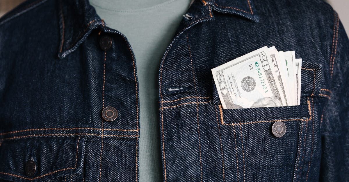 Difference of changing USD currency for going to US versus somewhere else - Crop unrecognizable male in casual outfit standing with different nominal pars of dollar banknotes in pocket of jeans jacket