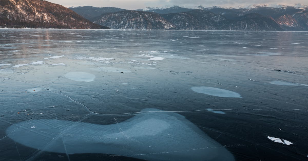 Do airlines have substantially different policies regarding adverse weather conditions? - Picturesque mountains and icy lake with blots on surface