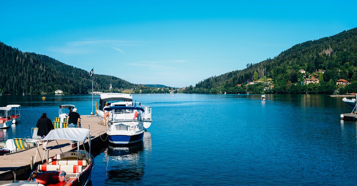 Do airlines have substantially different policies regarding adverse weather conditions? - Anonymous people walking on pier near different modern boats on tranquil water of river surrounded with slopes covered with forest