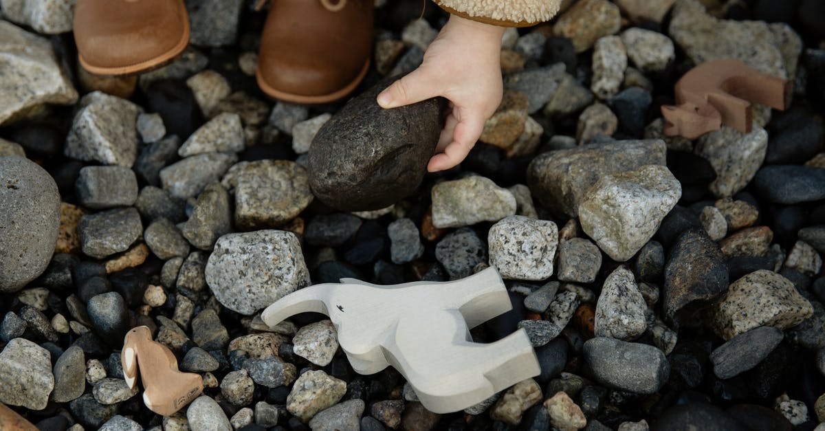 Do airlines typically charge for seating assignments when traveling w/ a small child? - Unrecognizable crop kid playing with toys and stones on rocky ground