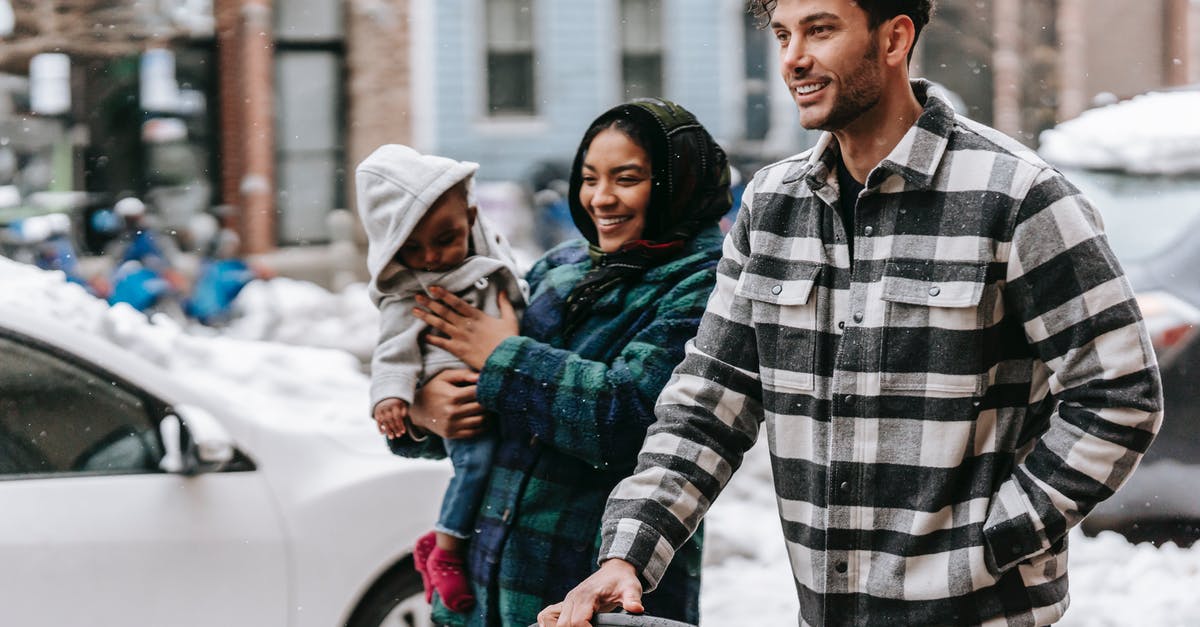 Do I have to carry snow chains in Europe? - Cheerful young diverse family with toddler strolling on street and smiling Do I have to carry snow chains in Europe? - Cheerful young diverse family with toddler strolling on street and smiling