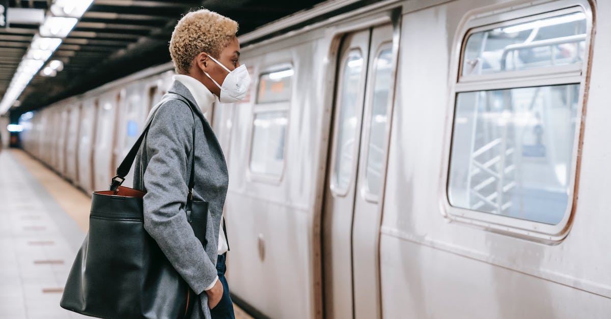 Do I need a transit visa at Haneda when self transferring? - Side view of unrecognizable confident young black female entrepreneur with short blond hair in elegant outfit and face mask standing in front of train in metro station