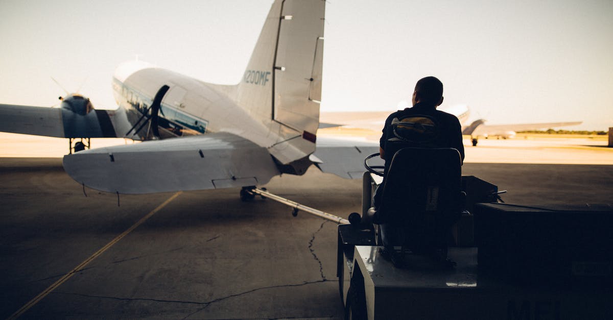 Do I need a transit visa at Haneda when self transferring? - Silhouette of worker driving baggage carrier on paved airfield with airplane before flight