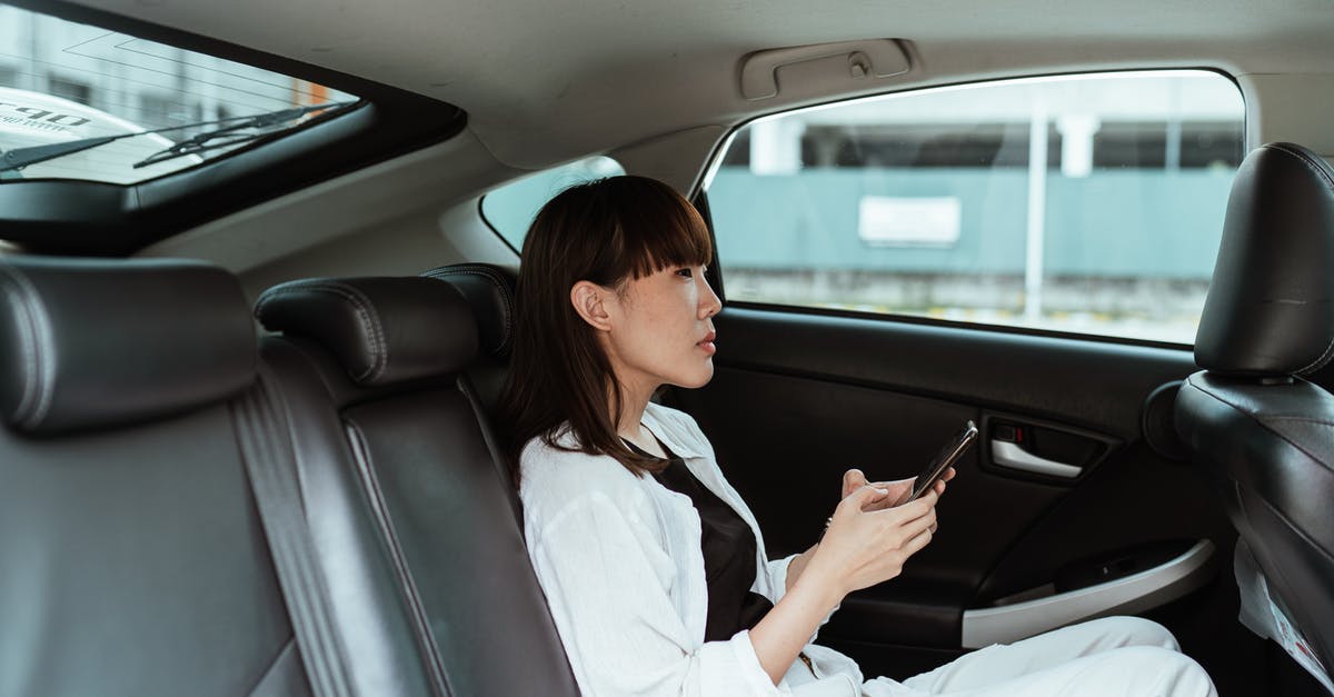 Do I need to include details about a side trip to another country on my Schengen application form? - Side view of focused young Asian female wearing casual white clothes and using modern smartphone while riding at car backseat
