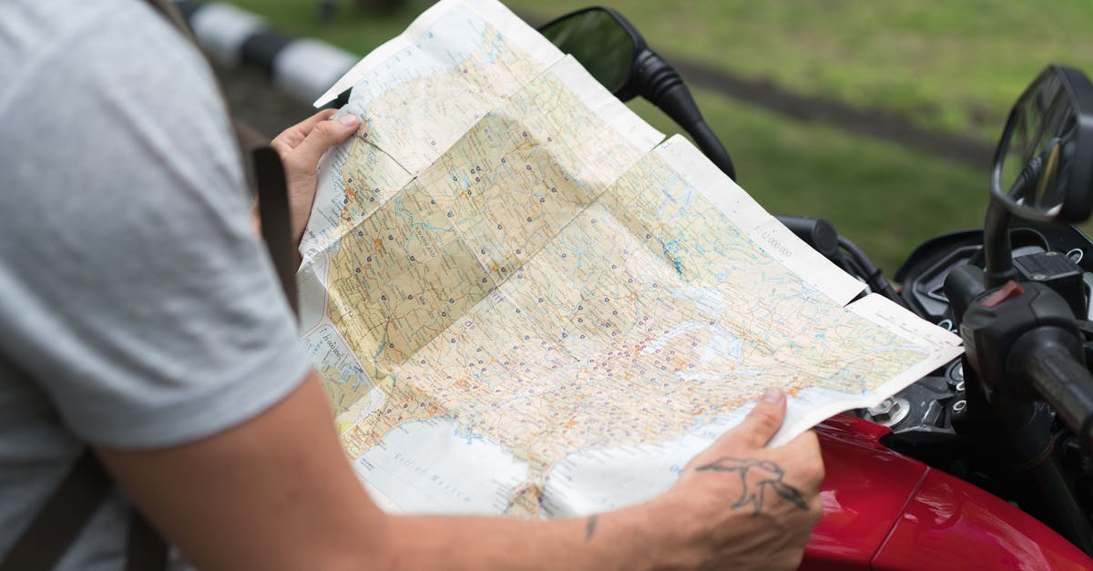 Do I need to include details about a side trip to another country on my Schengen application form? - Side view of crop unrecognizable male in casual clothes with backpack sitting on motorcycle while studying city map on street
